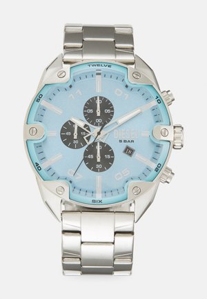 Montre en acier inoxydable argenté avec un cadran bleu, de grands chiffres, trois sous-cadrans noirs et une fenêtre de date. Résistante à l'eau jusqu'à 5 bars.