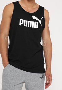 Musta puuvillainen hihaton toppi, jossa suuri valkoinen "PUMA"-logo ja pumagrafiikka. Yhdistetty harmaiden verkkareiden kanssa, molemmissa logoyksityiskohtia.