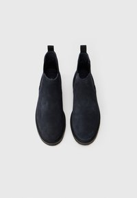Une paire de bottines en croûte de cuir bleu marine avec des semelles noires, vue de dessus sur un fond blanc.