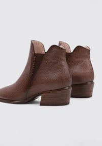 Botas de tobillo de cuero marrón con un acabado texturizado, que cuentan con un tacón bajo apilado y lados cortados. Interior en beige.