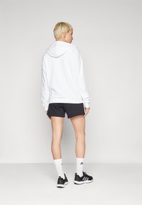 Hvit hettegenser med hette brukt sammen med svarte shorts. Mykt stoff med en avslappet passform. Svarte sko med hvite detaljer og hvite ankelsokker.