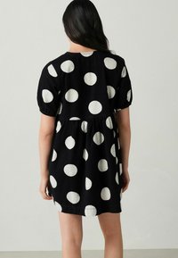 Musthave musta kleit suurte valgete polka punktidega, lühikeste puhvärvidega, kitsendatud taljega ja voogava seeliku osaga, valmistatud kergest materjalist.