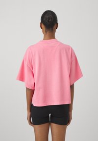 Růžové oversized tričko s krátkým rukávem, vyrobené z měkké bavlny. Má kulatý výstřih a volný střih, nošeno s černými šortkami.