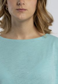 Top azzurro chiaro a maniche corte con una texture morbida, scollatura ampia e sottili linee orizzontali, posizionato su uno sfondo neutro.