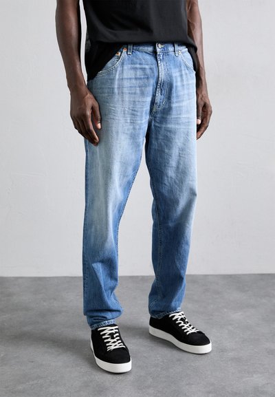 Jean bleu clair en denim, avec une coupe décontractée, des détails décolorés, cinq poches et des accessoires en métal, associés à des baskets noires.