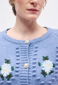 Ανοιχτό μπλε πλεκτή ζακέτα με κεντήματα λουλουδιών, στρογγυλό �κουμπί από πέρλα, ραβδωτή υφή και λεπτομέρεια γιακά με κυματιστό περίγραμμα.