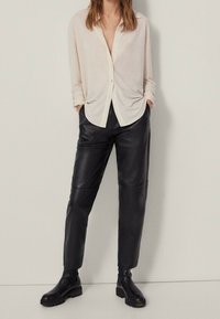 Light beige button-up shirt, relaxed fit, with rolled sleeves; black leather pants, tapered design, and chunky black boots.