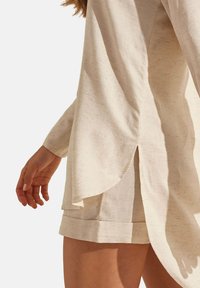 Lichtbeige linnen top met een zijslit en opgerolde mouwen, gecombineerd met bijpassende shorts met een omgeslagen zoom. Zachte textuur, casual ontwerp.