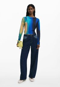Colorful long-sleeve top with blue, green, and orange gradients; paired with high-waisted navy sparkly wide-leg jeans and a small yellow bag.