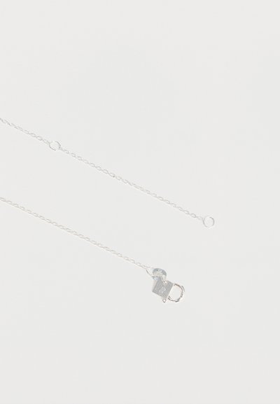Collier chaîne en argent délicat avec un petit fermoir rectangulaire et une boucle pour fixer sur un fond blanc uni.