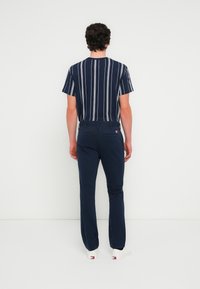 Κοντομάνικο πουκάμισο με ναυτικές ρίγες σε λευκό και γκρι, σετ με μπλε παντελόνι, και τα δύο από λείο ύφασμα. Ορατά λευκά αθλητικά παπούτσια.