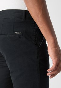 Zwarte katoenen broek met een slim fit, voorzien van zijzakken en een achterzak met een merketiket. Glad textuur en strakke lijnen.