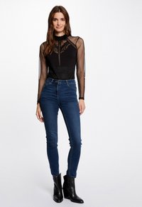 Black mesh bodysuit with long sleeves, floral lace design, and a high neck paired with dark blue skinny jeans and black ankle boots.