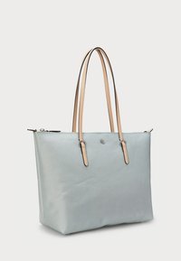 Saco de ombro azul claro feito de material texturizado, com duas alças de pele castanha, fecho com zip e um logótipo prateado à frente.