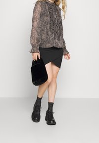 Blusa nera a fantasia con maniche voluminose, abbinata a una gonna nera asimmetrica. Gli accessori includono una borsa nera in pelliccia sintetica e scarpe nere spesse.