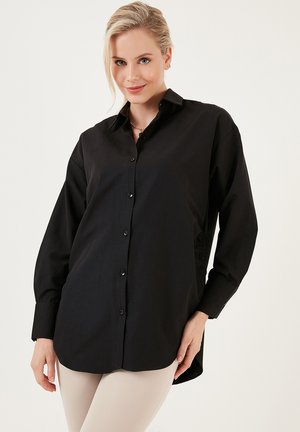 Zwarte overhemdsblouse gemaakt van zachte stof, met een klassieke kraag, lange mouwen en een relaxte pasvorm met een licht gebogen zoom.