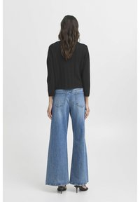 Černý cropped pletený svetr s ribovanou texturou doplněný o světle modré džíny s širokými nohavicemi. K outfitu ladí černé vysoké podpatky.