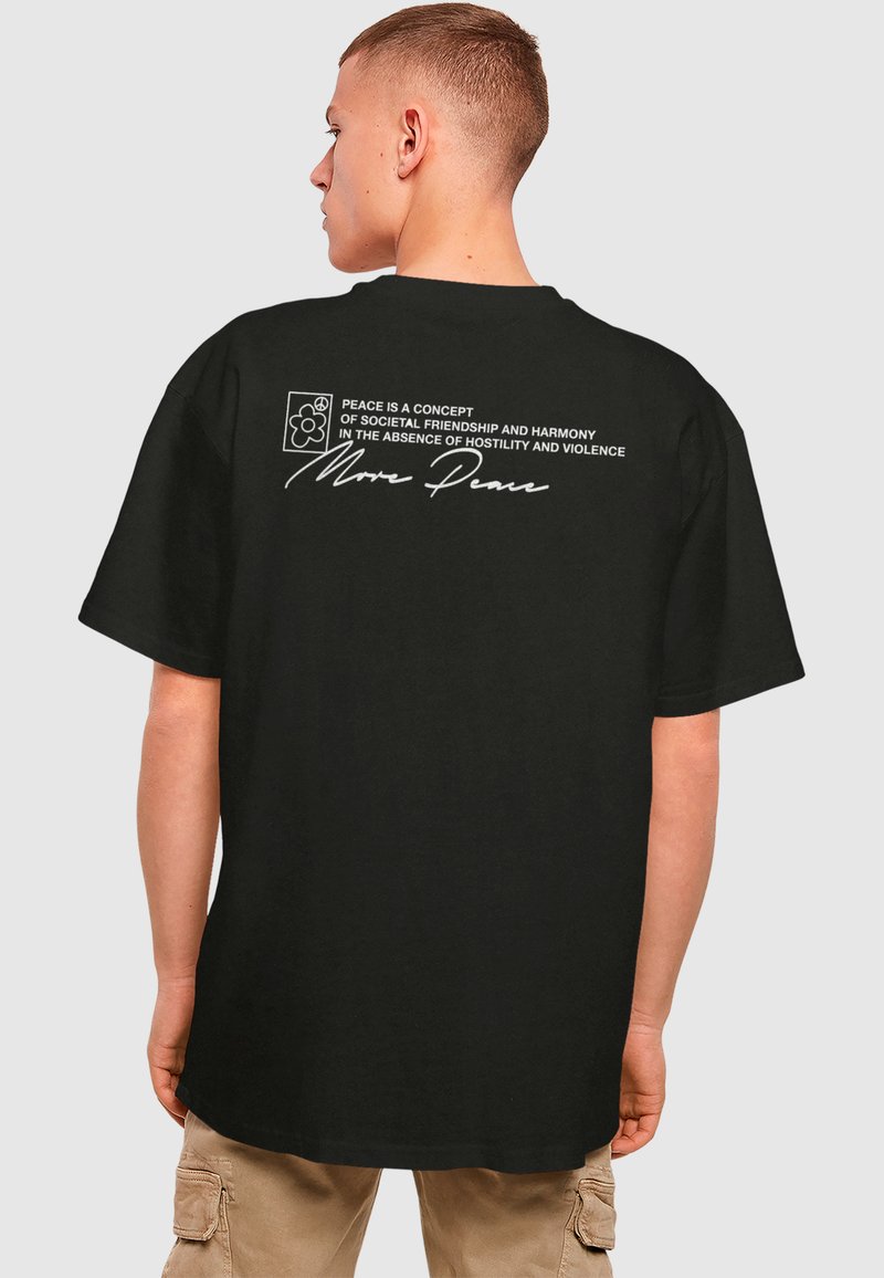 Sort bomulds T-shirt med et stort hvidt tekstgrafik på ryggen, som siger "Mere fred" sammen med yderligere tekst om samfundsmæssig harmoni og et blomsterikon.