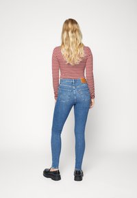 Jeans skinny de mezclilla azul con cintura alta y bolsillos traseros, combinados con una blusa de manga larga a rayas rojas y blancas. Textura suave.