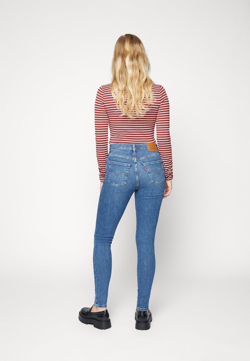 Blaue Skinny-Jeans aus Denim mit hoher Taille und Gesäßtaschen, kombiniert mit einem rot-weiß gestreiften Langarmshirt. Glatte Textur.