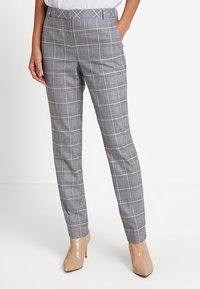 Pantalon à carreaux gris avec une coupe ajustée, présentant une texture lisse, des poches avant et une ceinture. Associé à des talons hauts nude.