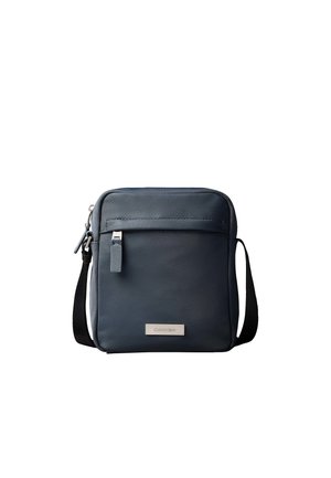 Compact dark grey crossbody bag with front zip pocket, adjustable black strap, and small brand logo plaque on front.
