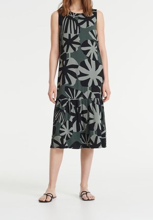 Robe sans manches avec un design à volants, ornée de grands motifs floraux noirs sur un fond vert. Fabriquée en tissu léger.