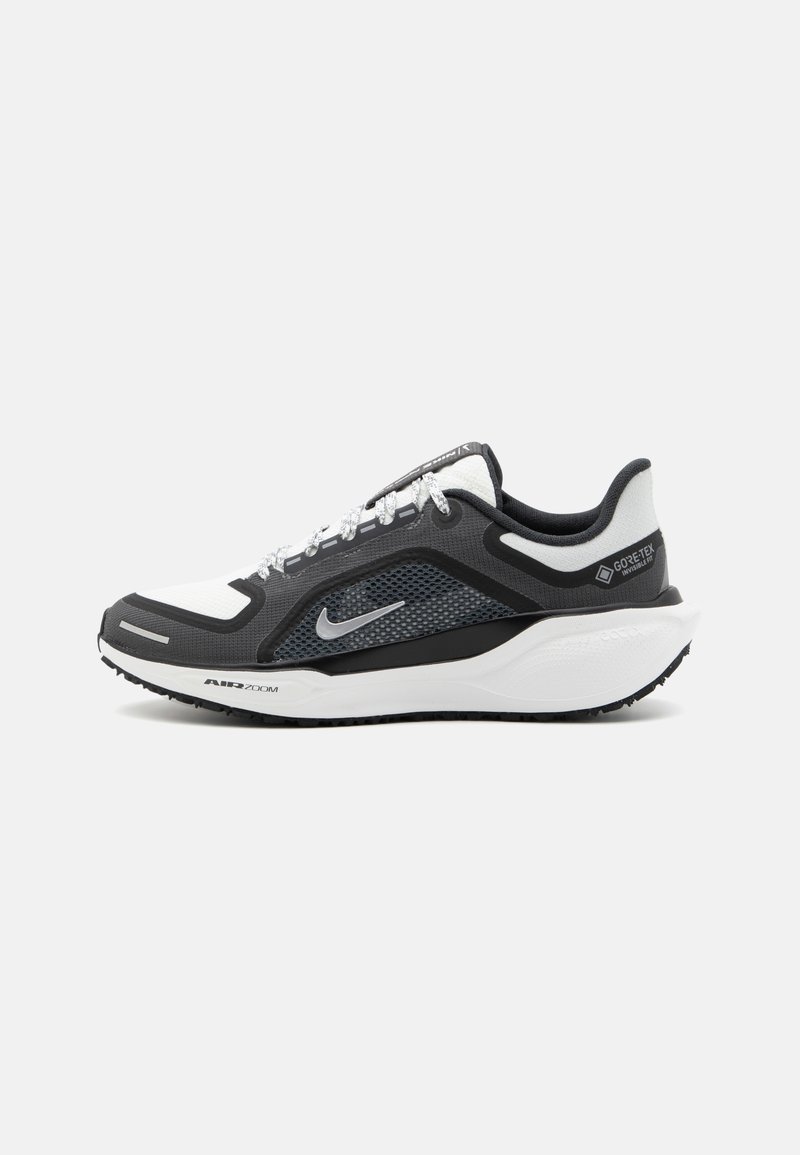 Nike sneakers with a black and white color scheme, mesh upper, and silver accents. Rubber sole with "Air Zoom" branding, textured for grip.