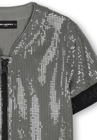 Haut gris pailleté avec un col rond, fermeture éclair et manches courtes. Présente une bande noire unie avec "KARL" imprimé en blanc.