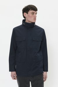 Chaqueta impermeable azul marino con un alto cuello, cremallera frontal y dos grandes bolsillos en el pecho. Textura suave y diseño minimalista.