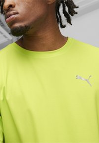 Camisa de manga corta verde neón con un patrón texturizado, que presenta un pequeño logo gris de Puma en el área izquierda del pecho.