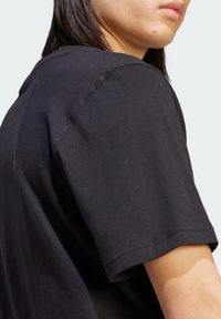 Camiseta de algodón negra con cuello en pico, mangas cortas y una textura suave. Detalle de costura en contraste visible en la costura del hombro.
