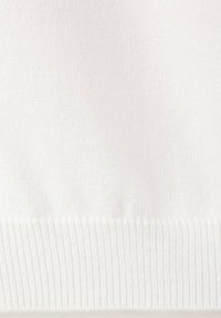 Gros plan d’un tissu blanc doux avec un motif tricoté côtelé le long du bord inférieur.