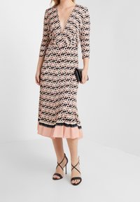 Šaty mají hluboký výstřih do V, tříčtvrteční rukávy, geometrický vzor v růžové a černé barvě, rozšířený lem s kontrastním černým páskem a hladký materiál.