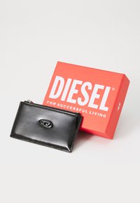 Black, glossy wallet with a textured surface and a raised oval logo at the center, placed beside a bright red packaging box with bold white text.
