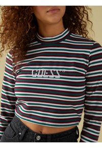 Lyhythihainen pitkähihaisen pusero, jossa on vaaleanpunaisia, vihreitä ja valkoisia raitoja; rintamuksessa brodeerattu "GUESS"-logo; pehmeä ja joustava kangas.