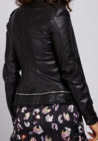 Černá kožená bunda s texturovanými panely na ramenou a svislými švy. Má stříbrný zip v pase a elegantní střih.