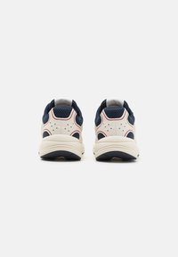 Zapatillas deportivas con un cuerpo color crema, acentos en azul marino y paneles de malla texturizada. Presenta un talón acolchado y una suela de goma con surcos para mayor tracción.