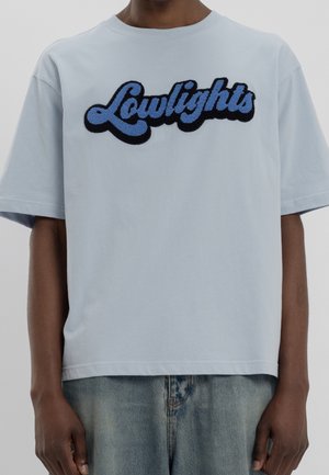 Helles blaues Baumwoll-T-Shirt mit kurzen Ärmeln, auf der Vorderseite mit schwarzem und blauem strukturiertem "Lowlights"-Stickerei versehen. Lässige Passform.