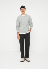 Pull léger gris à texture avec un col rond blanc, associé à un pantalon ample gris foncé et des baskets beiges avec des accents marron.