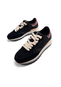Baskets noires avec un dessus texturé, présentant des lacets crème et un accent violet au niveau du talon. La semelle est légère avec une légère élévation.