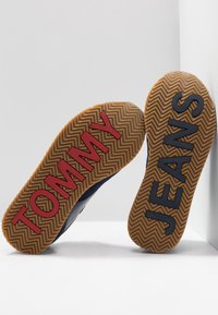 Baskets avec des semelles en caoutchouc texturé. "TOMMY" en rouge et "JEANS" en bleu marine, avec un motif en chevrons. Partie supérieure en matériau bleu foncé.
