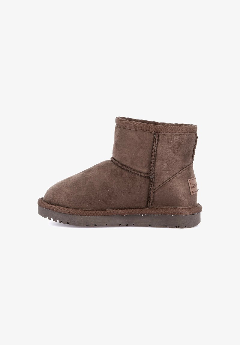 Stivale alla caviglia in suede marrone con cuciture a vista, suola piatta in gomma e una piccola etichetta del marchio nella zona del tallone su uno sfondo bianco.