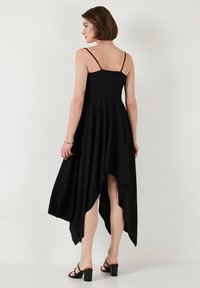 Čierne šaty s priliehavým telom, tenkými ramienkami a vysokou nízkou manžetou. Mäkko, splývavé tkaniny sa elegantne vlnia, zdôrazňujú pohyb.