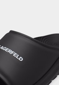 Μαύρο σανδάλι με φαρδιά λουράκι που φέρει το λογότυπο "KARL LAGERFELD" σε λευκό χρώμα και ανάγλυφη σόλα ορατή στο φόντο.
