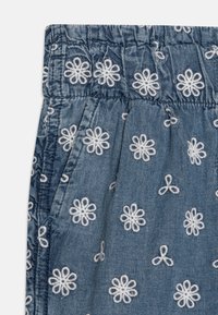 Plava tkanina s bijelom cvjetnom aplikacijom, elastičan pojas i džepovi. Tekstura je meka s malo naboranim izgledom.