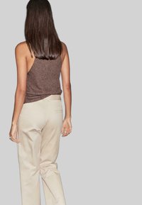 Bruine gebreide tanktop gecombineerd met beige op maat gemaakte broeken, vanuit de achterkant weergegeven, met een ontspannen pasvorm en minimale details.