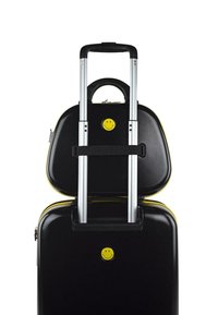 Maleta rígida negra con acentos amarillos, un sticker de una cara sonriente, dos asas de aluminio extensibles y un asa superior de transporte.