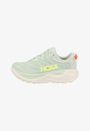 Scarpa da corsa HOKA verde chiaro con suola bianca spessa e linguetta arancione al tallone, con tomaia in mesh traspirante e design con lacci.