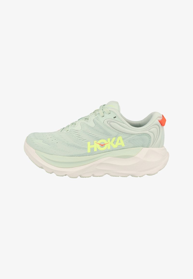 Scarpa da corsa HOKA verde chiaro con suola bianca spessa e linguetta arancione al tallone, con tomaia in mesh traspirante e design con lacci.